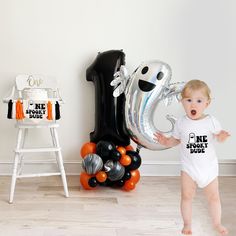 a baby standing next to a balloon shaped like a number