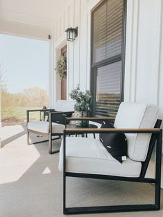 two white chairs sitting on top of a porch next to a table and potted plant