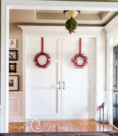 two wreaths hanging on the front door of a white room with wood floors and framed pictures