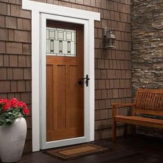 a white vase with red flowers sitting next to a wooden door on a brown house