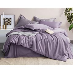 a bed with purple sheets and pillows in a room next to a potted plant