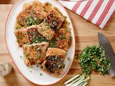 a white plate topped with meat covered in sauce and green onions on top of a wooden table