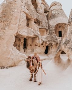 a woman standing next to a camel in front of some rocks and caves at the desert