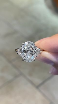 a woman's hand holding an oval diamond ring on top of a tile floor