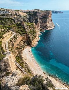 an aerial view of the beach and ocean near a cliff side resort in spain, with blue water