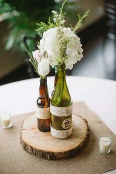 two bottles with flowers in them sitting on a wood slice at the center of a table