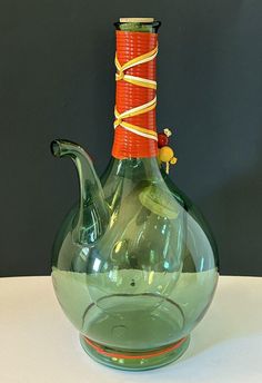 a green glass vase with a red handle and yellow string on the top is sitting on a white table