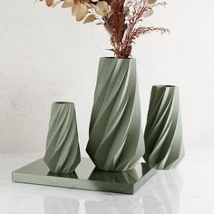 three green vases with flowers in them on a white tableclothed surface next to each other