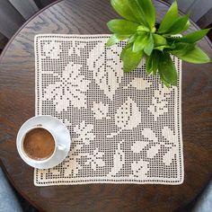 a cup of coffee sitting on top of a table next to a potted plant