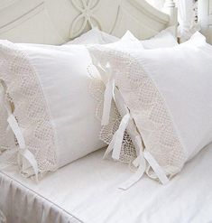 two white pillows sitting on top of a bed covered in white sheets and ruffles