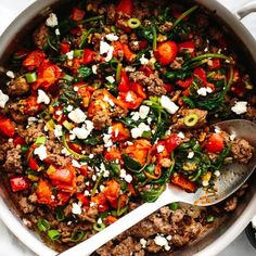 a pot filled with meat and vegetables on top of a white table cloth next to a spoon