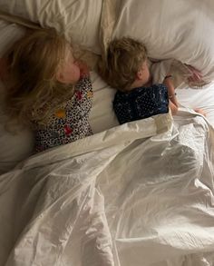 two young children laying in bed with white sheets and blankets on top of each other