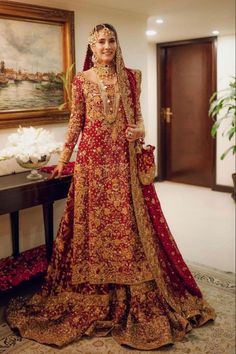 a woman in a red and gold bridal gown standing next to a painting on the wall