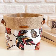 a close up of a bag on a table near a book and coffee cup with a brick wall in the background