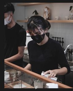 a woman wearing a face mask standing behind a counter in a restaurant while another man looks on