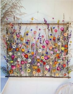 a wall hanging with flowers and plants on it in front of a white chair next to a planter