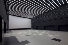 an empty room with black and white tiles on the floor in front of a large screen