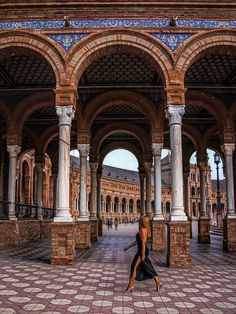 a woman is walking through an old building with columns and arches on the side walk