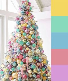 a colorful christmas tree with ornaments on it and presents under the tree, in front of a large window