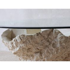 a table with a glass top and rock like structure on the bottom, sitting in front of a white wall