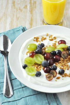 a white plate topped with yogurt and fruit next to a fork on a blue napkin