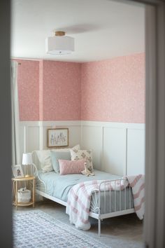 a bedroom with pink and white wallpaper, a bed in the corner and a rug on the floor