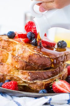 french toast with syrup being drizzled over it and berries on the side