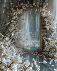 a mirror surrounded by white flowers in front of a curtained room with drapes