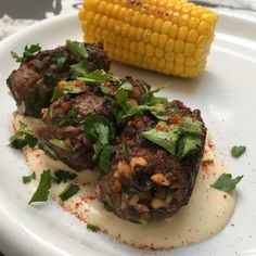 two meatballs on a white plate next to a corn cob and garnish