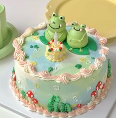 two green frogs sitting on top of a cake next to a cup and saucer