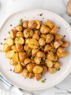 a white plate topped with cooked potatoes on top of a marble countertop next to a knife and fork