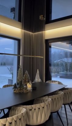 a dining room table surrounded by chairs with lights on them and snow outside the window