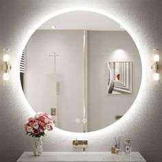 a bathroom with a round mirror on the wall and flowers in a vase next to it