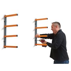 a man is working on a wall mounted shelf with two orange shelving racks and one holding a drill bit