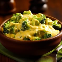 a wooden bowl filled with broccoli covered in cheese