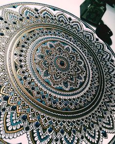 an intricately designed blue and gold plate on top of a white tablecloth with a black clock in the background