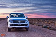 a silver car parked on the side of a dirt road in front of a sunset