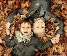 two young children laying on leaves in the middle of autumn time, looking up at the camera