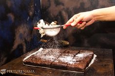 someone is sprinkling sugar on a chocolate cake