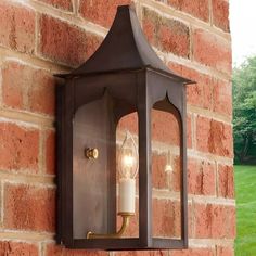 an outdoor wall light on the side of a brick building with a lit candle in it