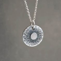 "Handmade sterling silver hammered disc necklace with a minimalist design. The pendant showcases a textured and oxidised surface, highlighting a small disc at its center. It gracefully hangs on a sterling silver trace chain. This symbolic handmade disc necklace serves as a reminder to find balance and stay centered. It makes the perfect gift for those seeking balance and harmony in their lives. With its meaningful design, it is especially cherished by yoga lovers and makes a thoughtful gift for friends, mothers, wives, girlfriends, or even as a special treat for oneself. Dimensions: Diameter of the disc approximately 1.5 cm (0.5\"). Metal: High quality 925 sterling silver The necklace will come in a beautiful branded gift box.  Each necklace is made by hand, ensuring that every piece posse Hammered Sterling Silver Coin Pendant Necklace, Silver Hammered Coin Necklace, Silver Hammered Round Disc Necklace, Hammered Sterling Silver Coin Necklace, Silver Hammered Round Coin Necklace, Hammered Round Sterling Silver Coin Necklace, Round Sterling Silver Hammered Coin Necklace, Minimalist Hammered Coin Necklace, Minimalist Hammered Round Coin Necklace