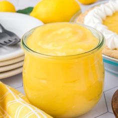 a glass jar filled with lemon custard on top of a table next to plates and spoons