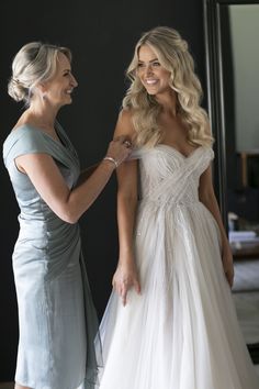 two women standing next to each other in front of a mirror wearing dresses and smiling