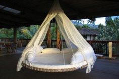 a white bed hanging from the ceiling in a room with wooden floors and palm trees