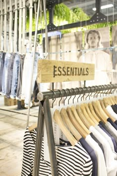 clothes hanging on racks in a store with an essential wood sign that says essentials