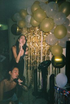 two women singing into microphones in front of balloons and streamers