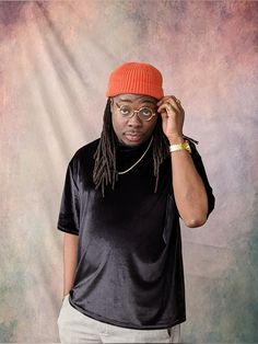 a man with dreadlocks and an orange hat is posing for a photo in front of a backdrop