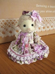 a small stuffed animal in a dress on a wooden table next to a card board