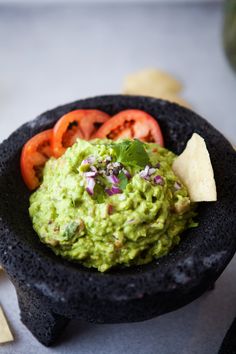 a black bowl filled with guacamole, tomatoes and tortilla chips