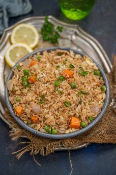 a bowl filled with rice and vegetables on top of a table next to lemon wedges